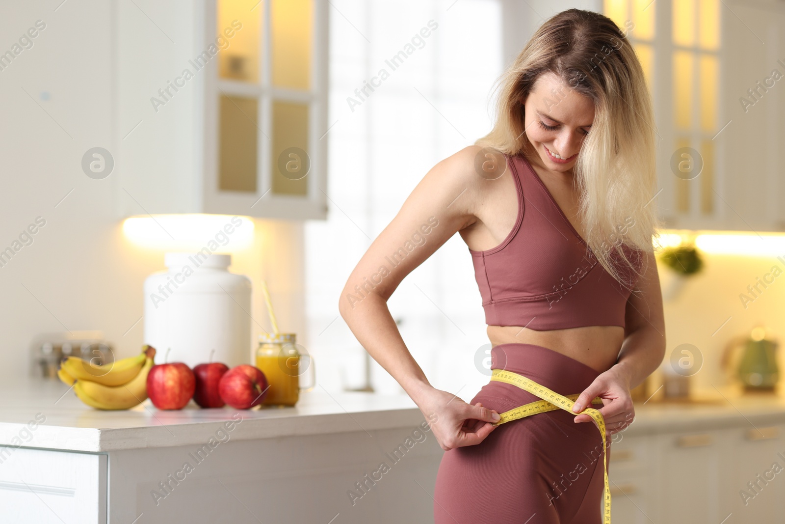 Photo of Weight loss. Woman measuring waist with tape in kitchen