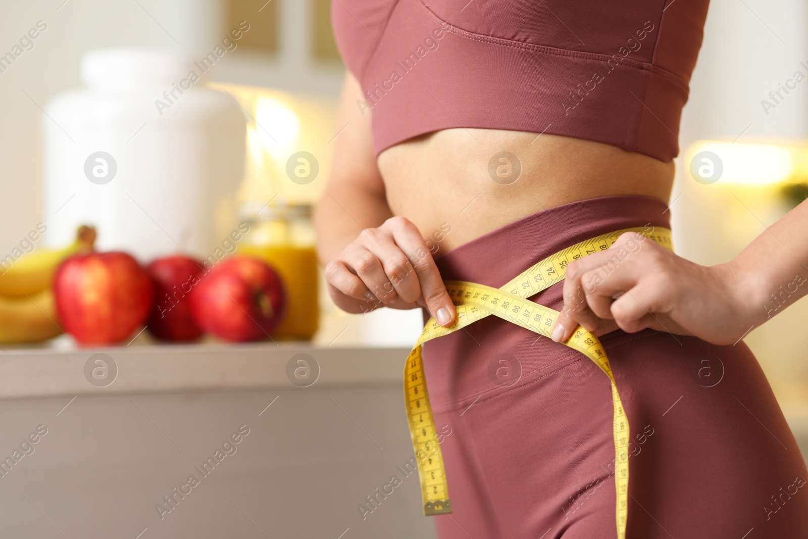 Photo of Weight loss. Woman measuring waist with tape in kitchen, closeup