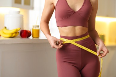 Photo of Weight loss. Woman measuring waist with tape in kitchen, closeup