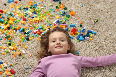 Photo of Cute girl lying near building blocks on carpet at home