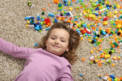 Photo of Cute girl lying near building blocks on carpet at home