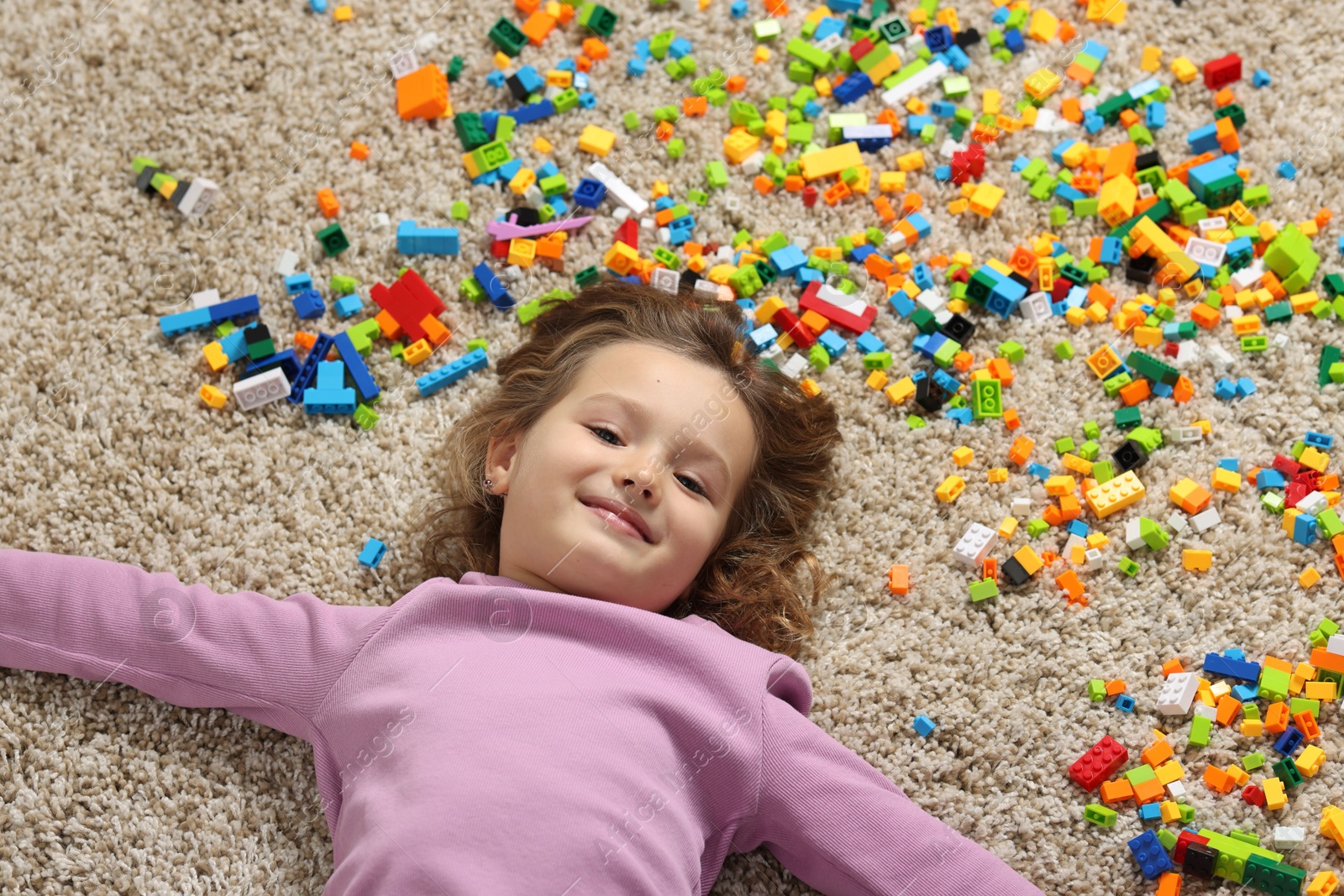 Photo of Cute girl lying near building blocks on carpet at home