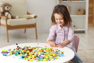 Photo of Cute girl playing with building blocks at white table indoors. Space for text