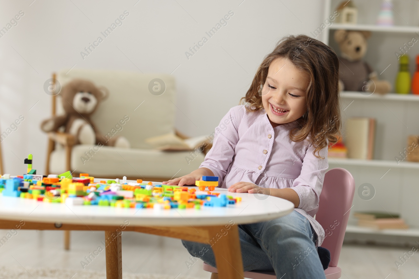 Photo of Cute girl playing with building blocks at white table indoors