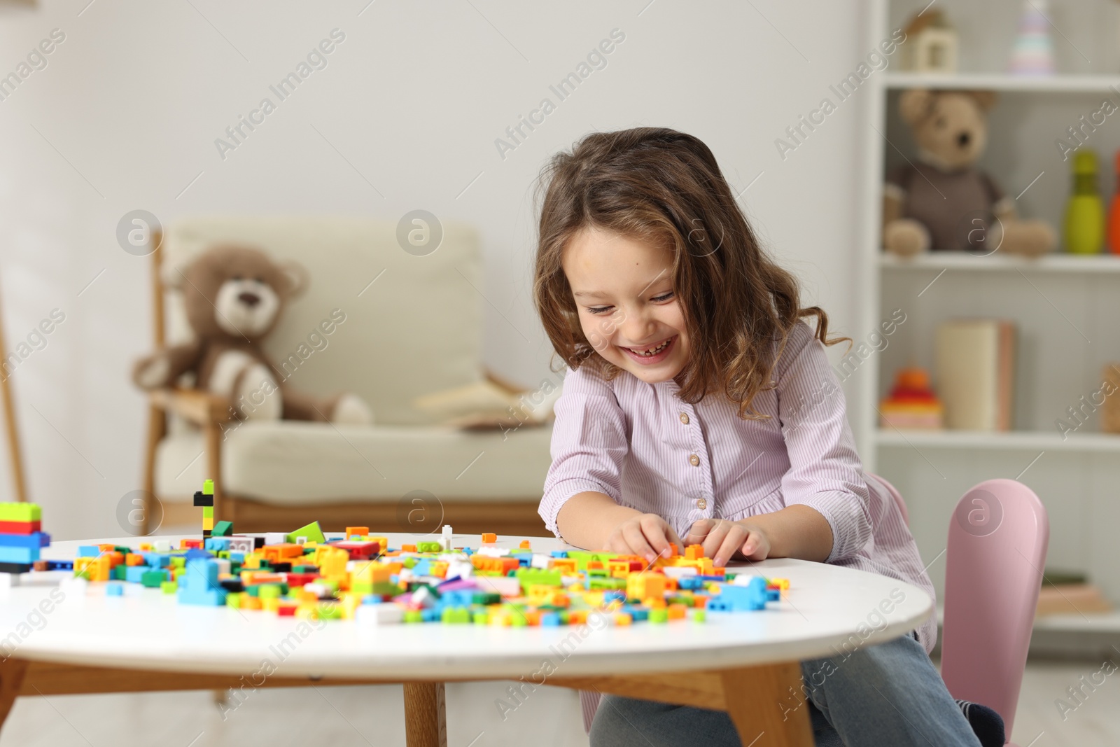 Photo of Cute girl playing with building blocks at white table indoors