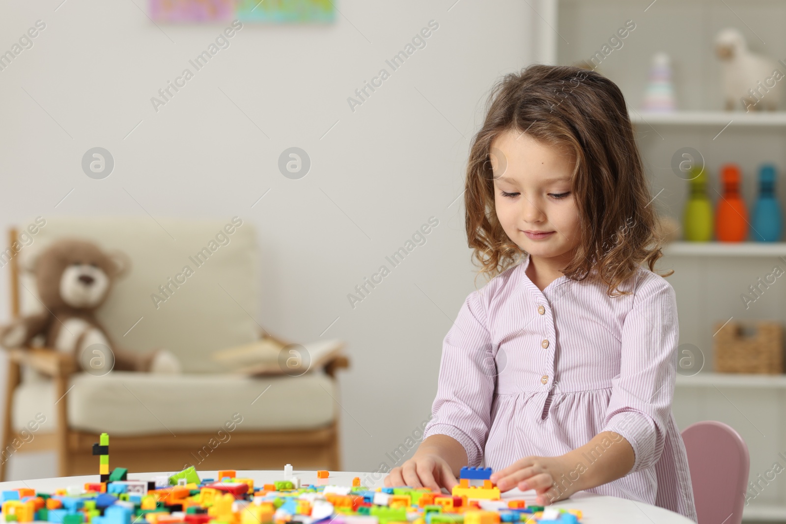 Photo of Cute girl playing with building blocks at white table indoors. Space for text