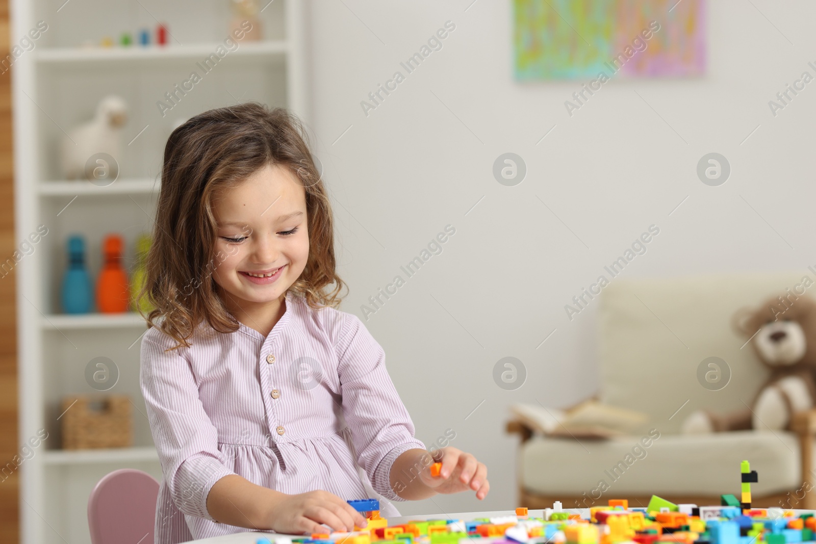 Photo of Cute girl playing with building blocks at white table indoors. Space for text