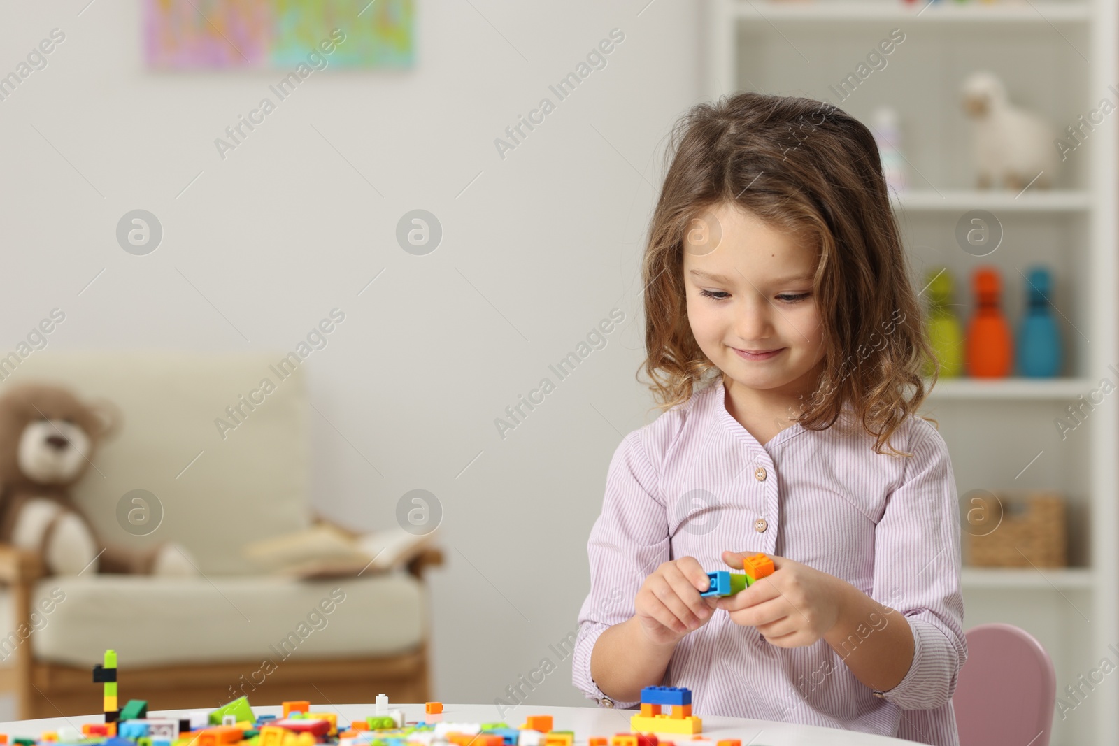 Photo of Cute girl playing with building blocks at white table indoors. Space for text