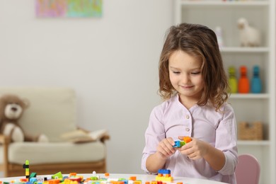 Photo of Cute girl playing with building blocks at white table indoors. Space for text