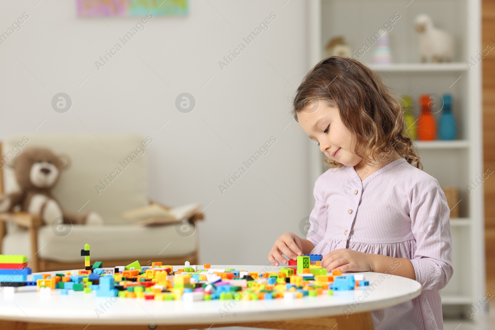 Photo of Cute girl playing with building blocks at white table indoors. Space for text