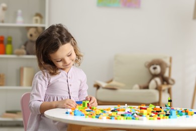 Photo of Cute girl playing with building blocks at white table indoors. Space for text