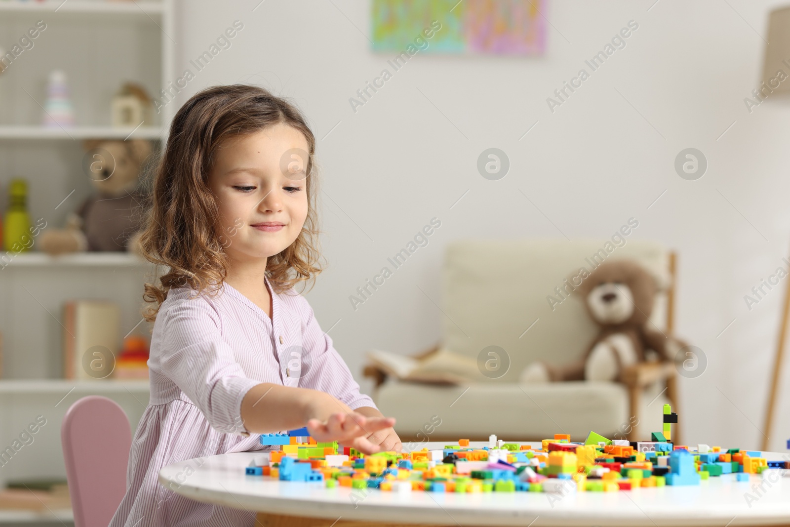 Photo of Cute girl playing with building blocks at white table indoors. Space for text