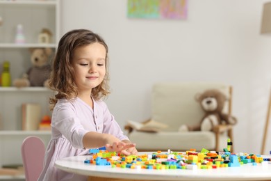 Photo of Cute girl playing with building blocks at white table indoors. Space for text