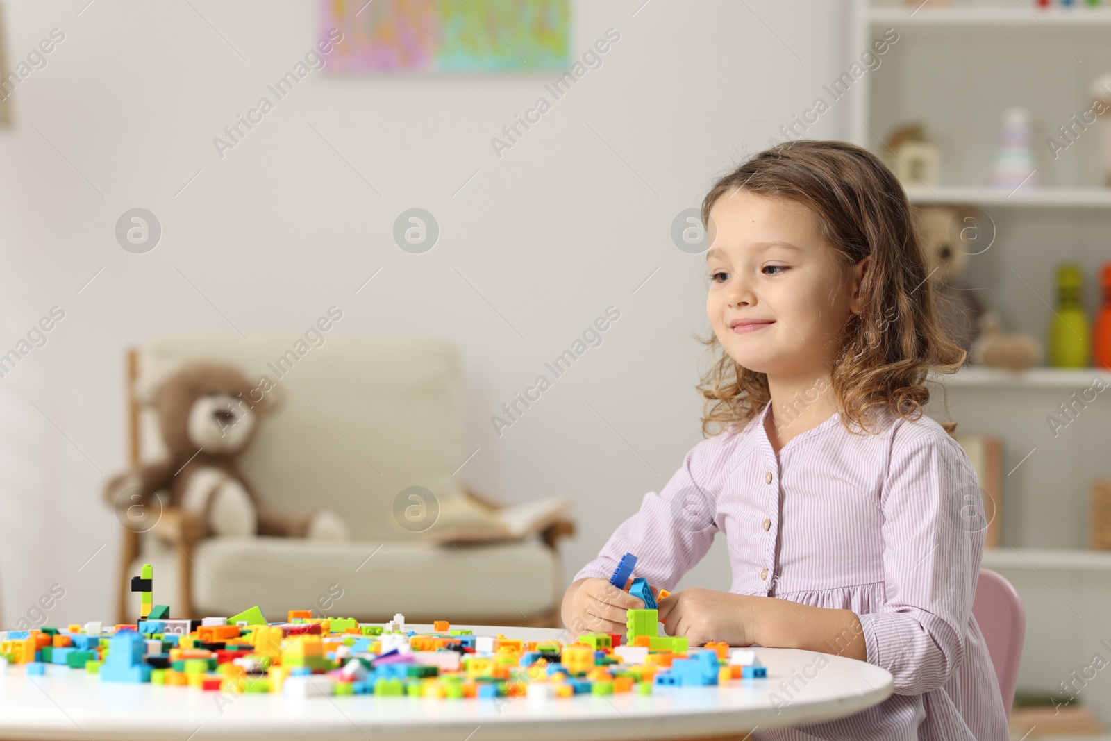 Photo of Cute girl playing with building blocks at white table indoors. Space for text