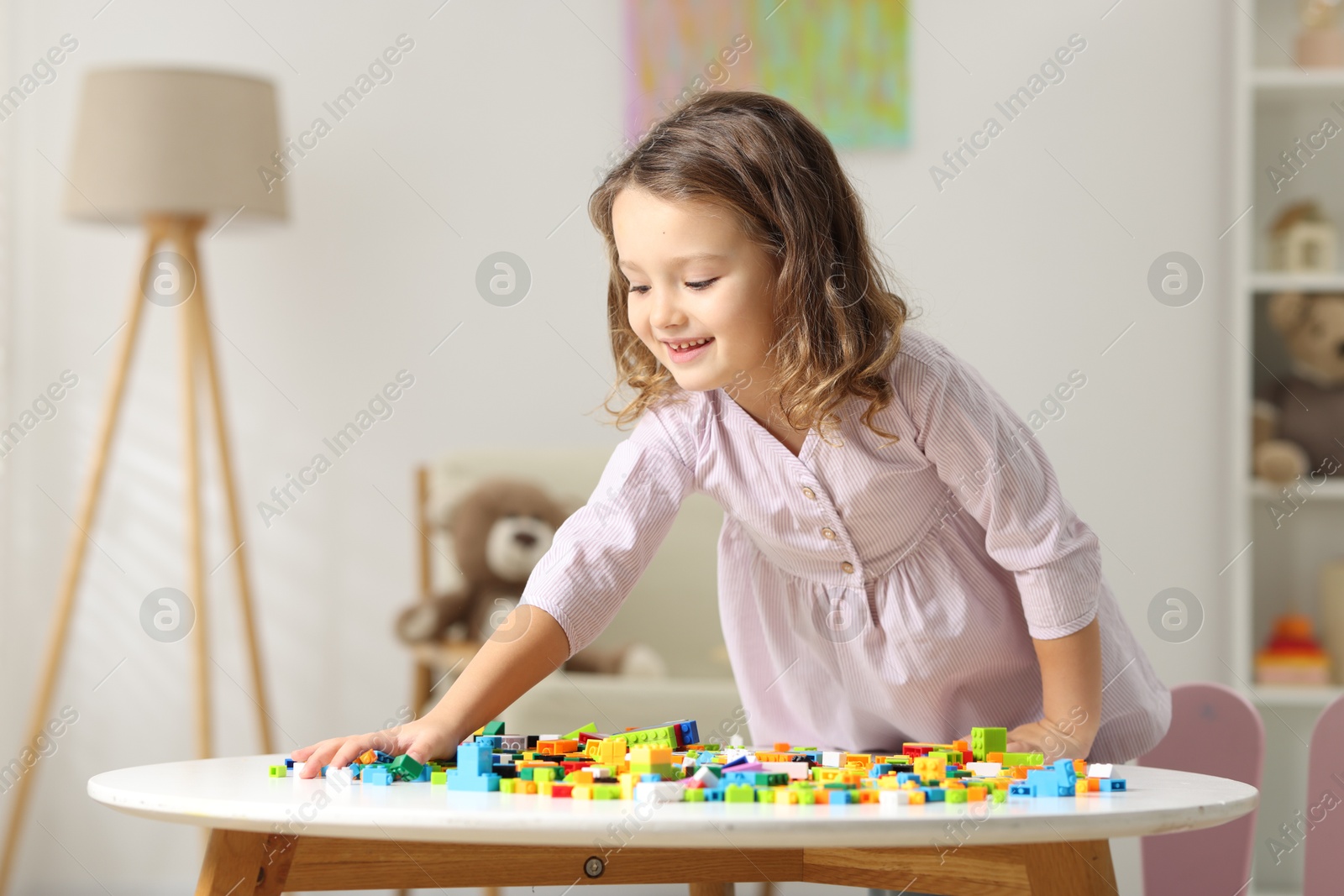 Photo of Cute girl playing with building blocks at white table indoors