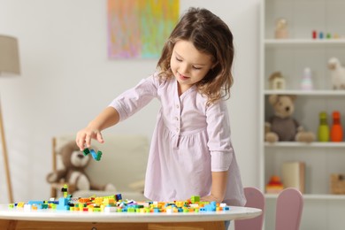 Photo of Cute girl playing with building blocks at white table indoors