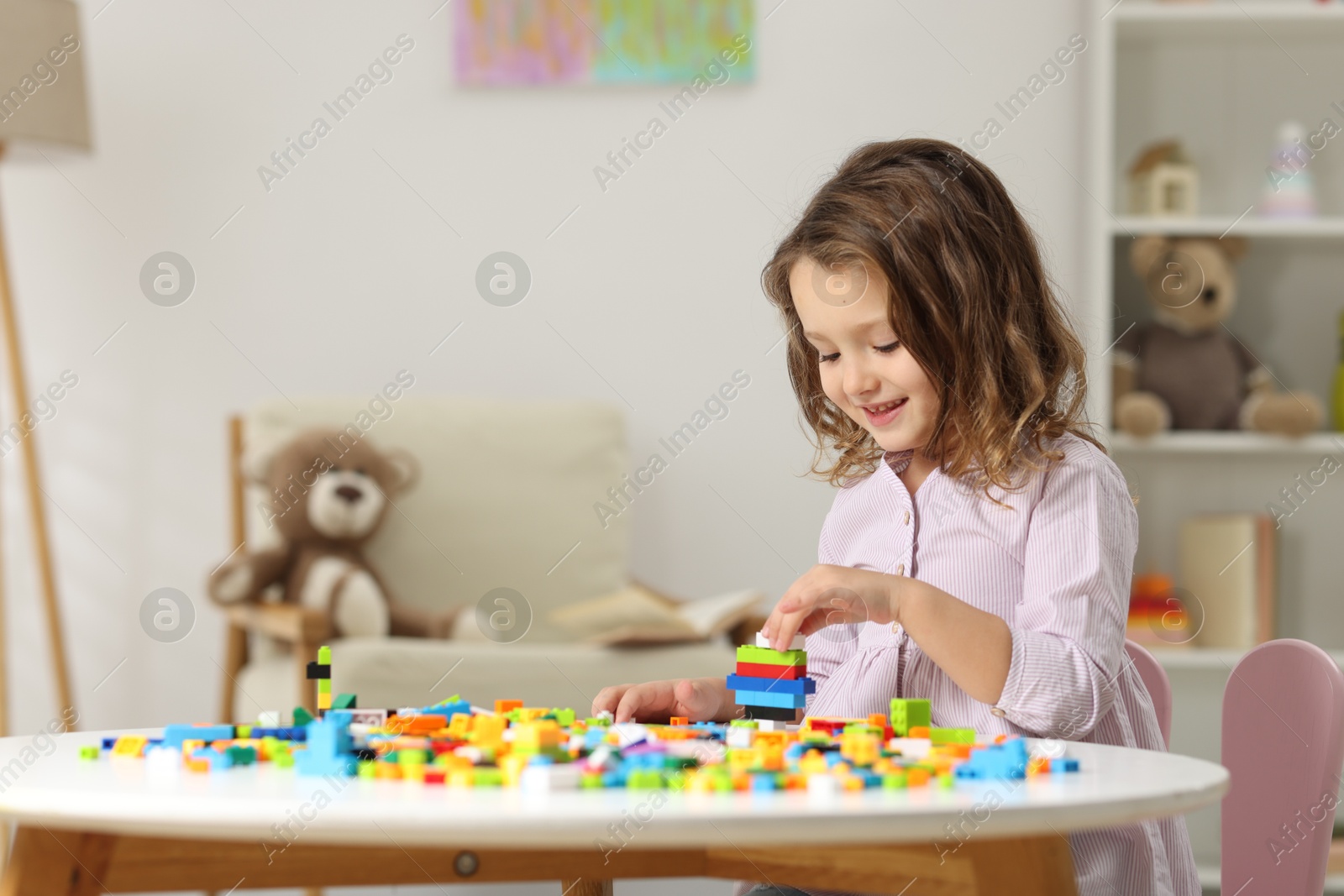 Photo of Cute girl playing with building blocks at white table indoors