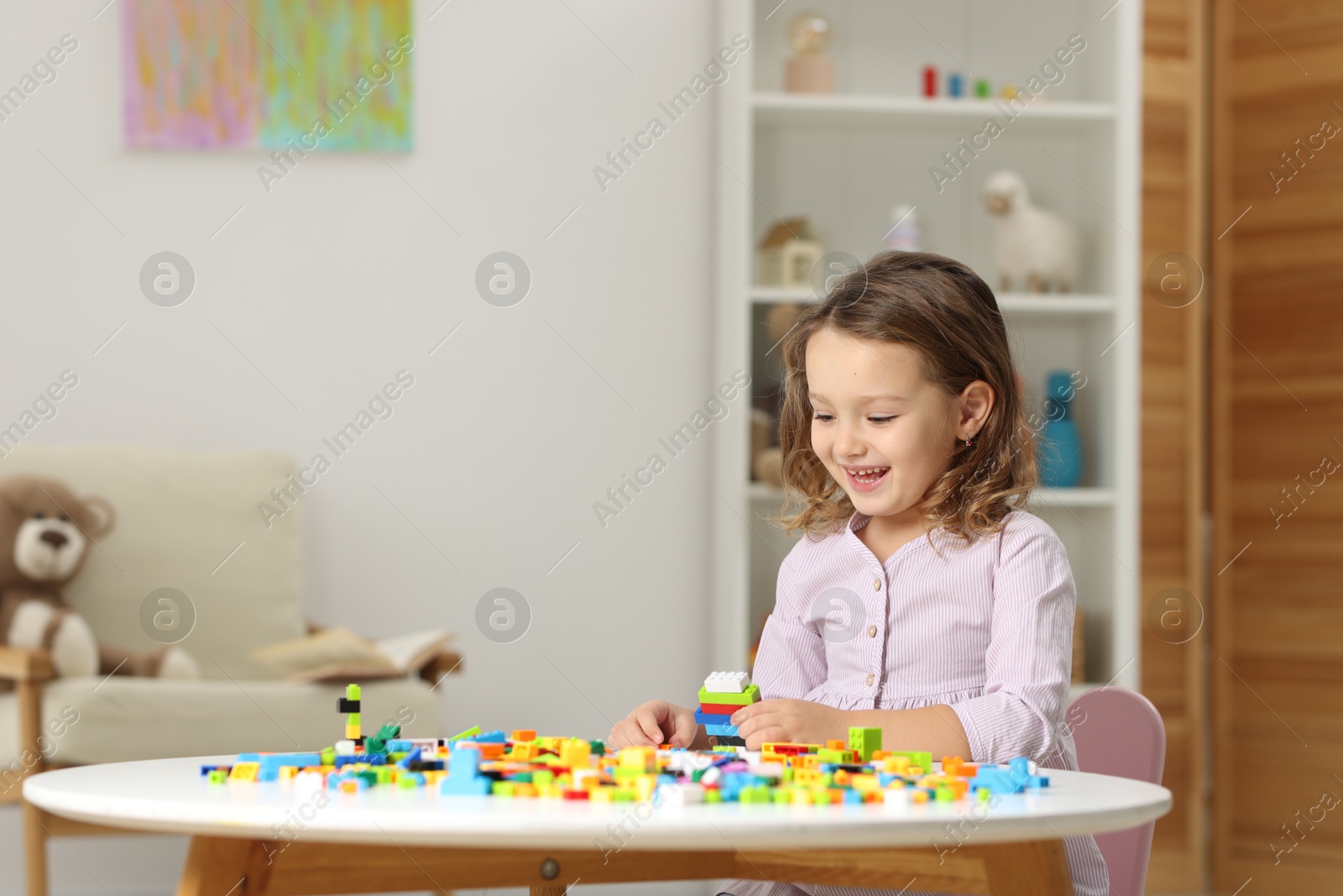 Photo of Cute girl playing with building blocks at white table indoors. Space for text