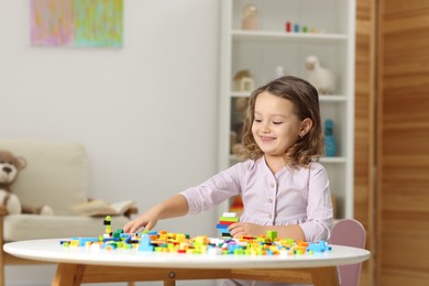 Photo of Cute girl playing with building blocks at white table indoors. Space for text