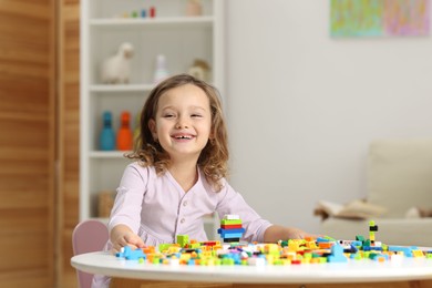 Photo of Cute girl playing with building blocks at white table indoors. Space for text