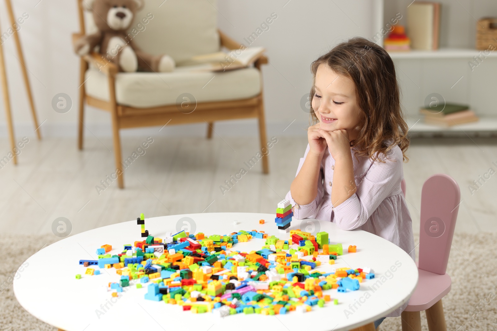 Photo of Cute girl playing with building blocks at white table indoors. Space for text