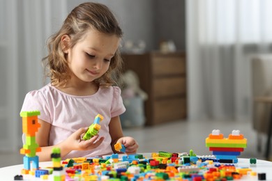 Photo of Cute girl playing with building blocks at white table indoors. Space for text