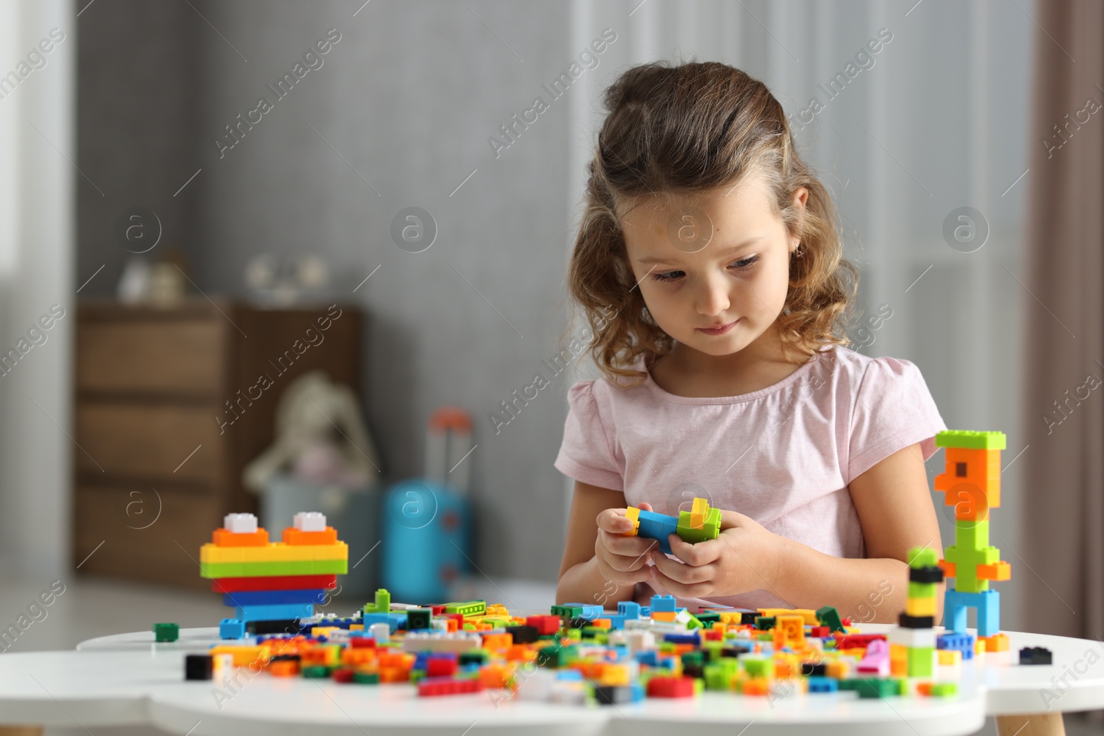 Photo of Cute girl playing with building blocks at white table indoors. Space for text