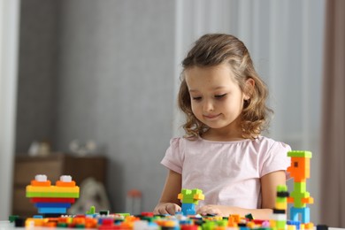 Photo of Cute girl playing with building blocks at white table indoors. Space for text