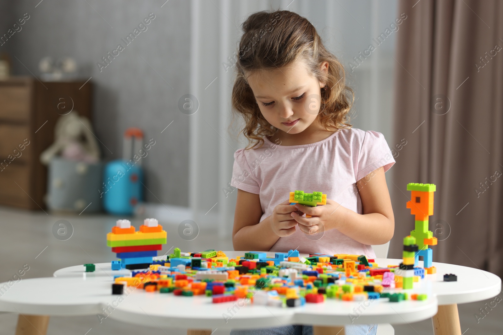 Photo of Cute girl playing with building blocks at white table indoors