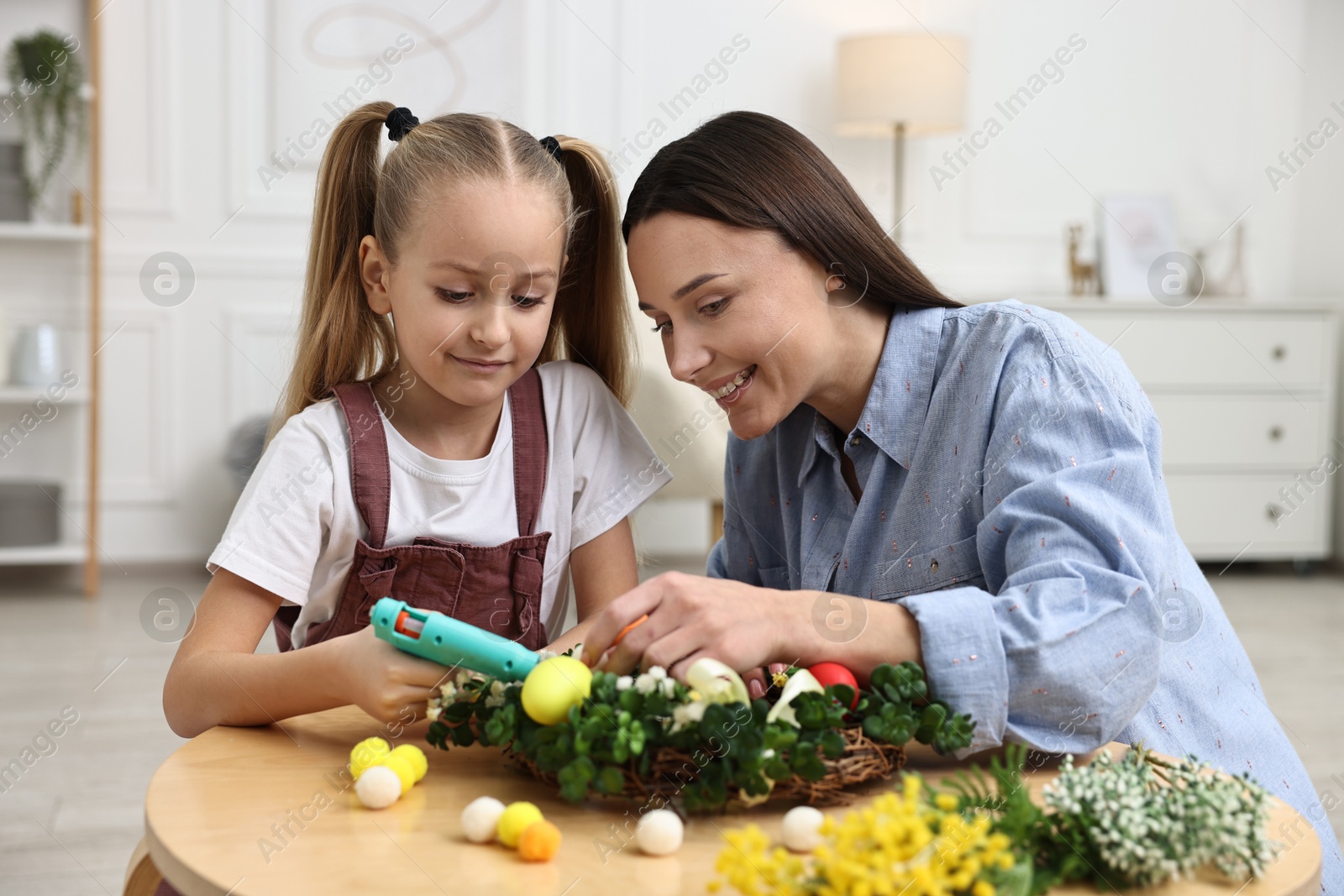 Photo of Mother and daughter with hot glue gun creating Easter composition at table indoors