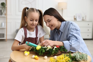 Photo of Mother and daughter with hot glue gun creating Easter composition at table indoors