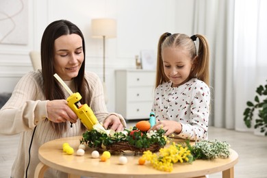 Photo of Mother and daughter with hot glue guns creating Easter composition at table indoors