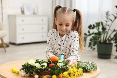 Photo of Little girl with hot glue gun creating Easter composition at table indoors