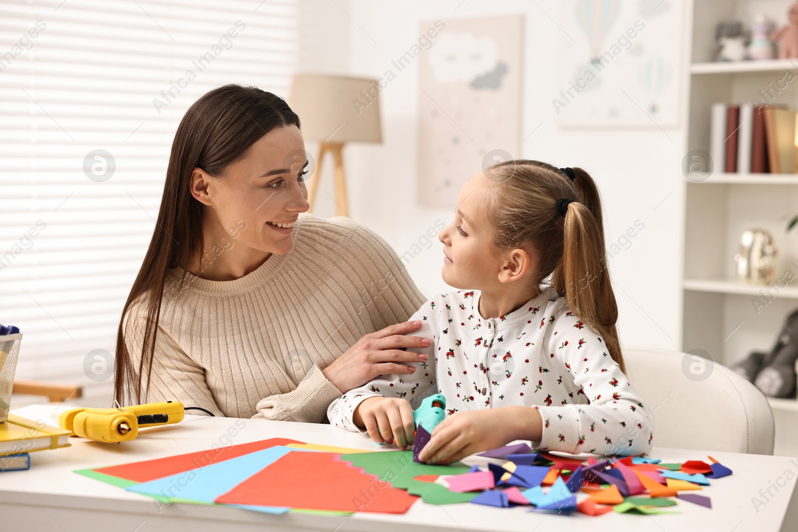 Photo of Mother and daughter with hot glue gun and color paper making craft at table indoors