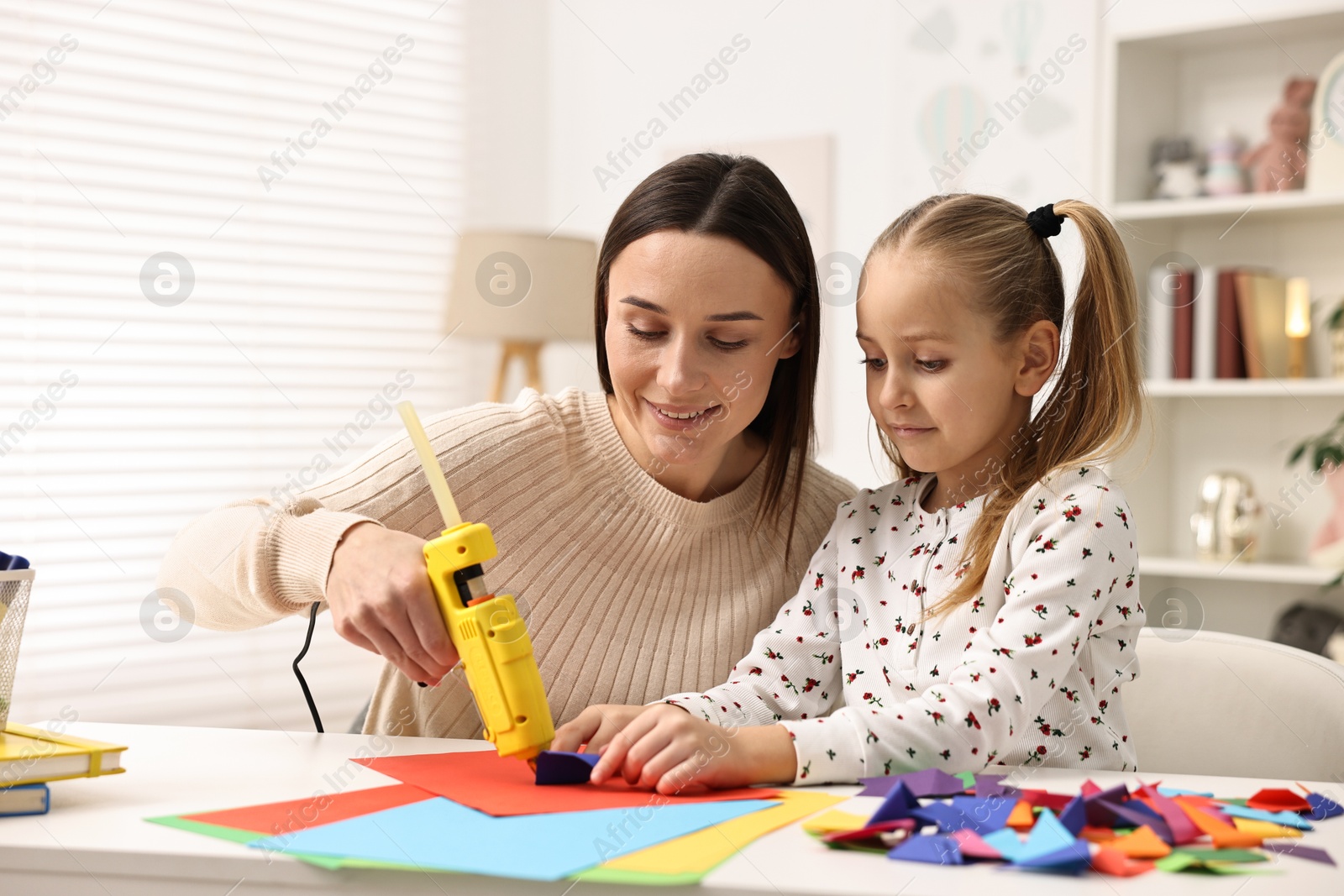 Photo of Mother and daughter with hot glue gun and color paper making craft at table indoors