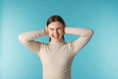 Photo of Frustrated woman covering her ears from loud noise on blue background