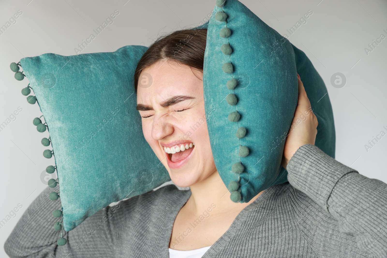 Photo of Distressed woman covering her ears with pillows from loud noise on light grey background