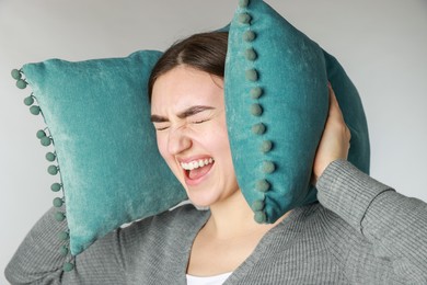 Photo of Distressed woman covering her ears with pillows from loud noise on light grey background