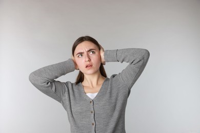 Photo of Distressed woman covering her ears from loud noise on light grey background