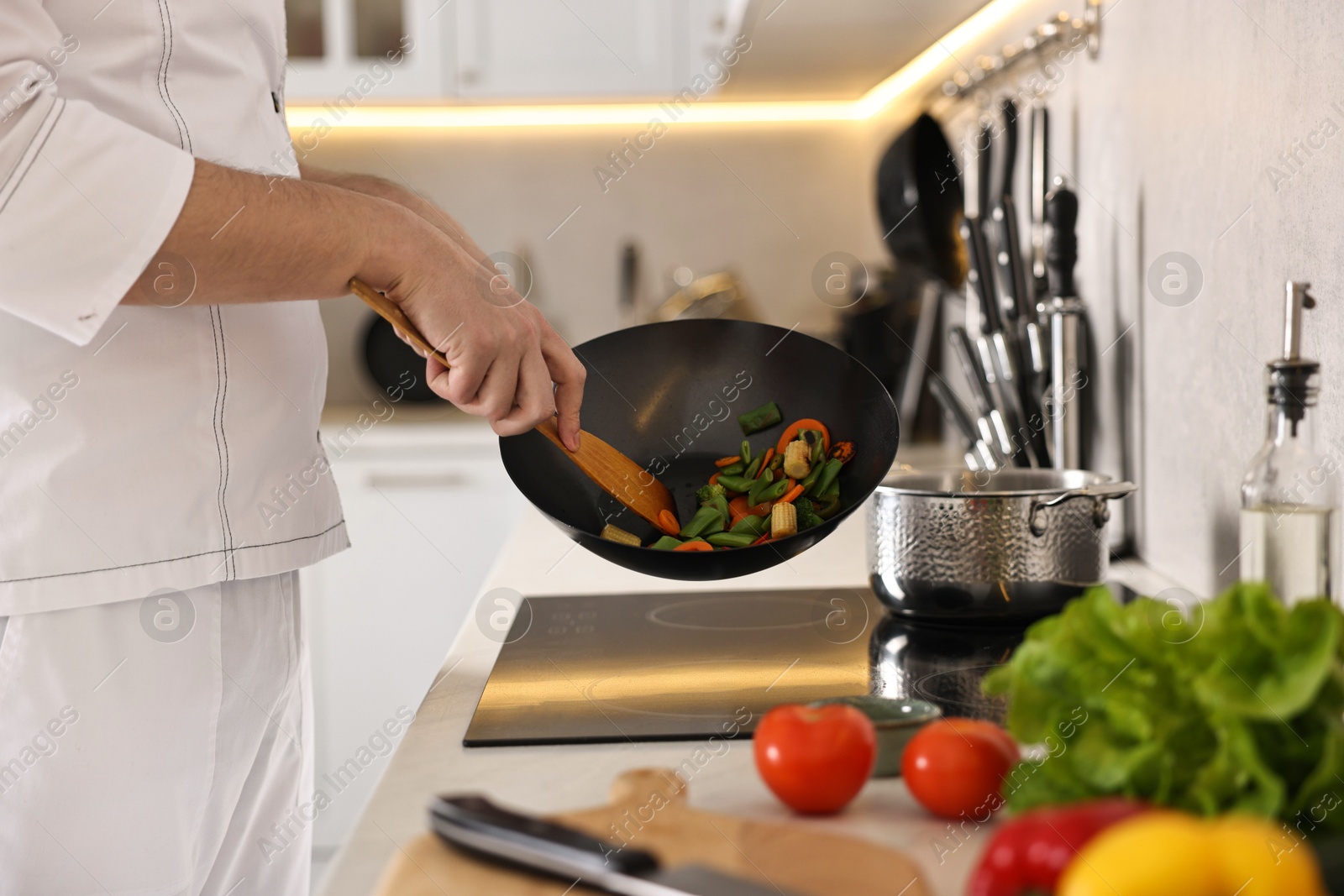 Photo of Professional chef mixing vegetables in wok at kitchen, closeup