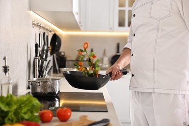 Photo of Professional chef mixing vegetables in wok at kitchen, closeup