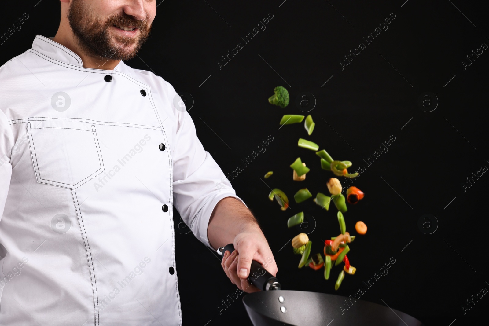 Photo of Professional chef mixing vegetables in wok on black background, closeup