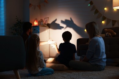 Photo of Shadow play. Father and his son making hand gestures like dogs on wall at home