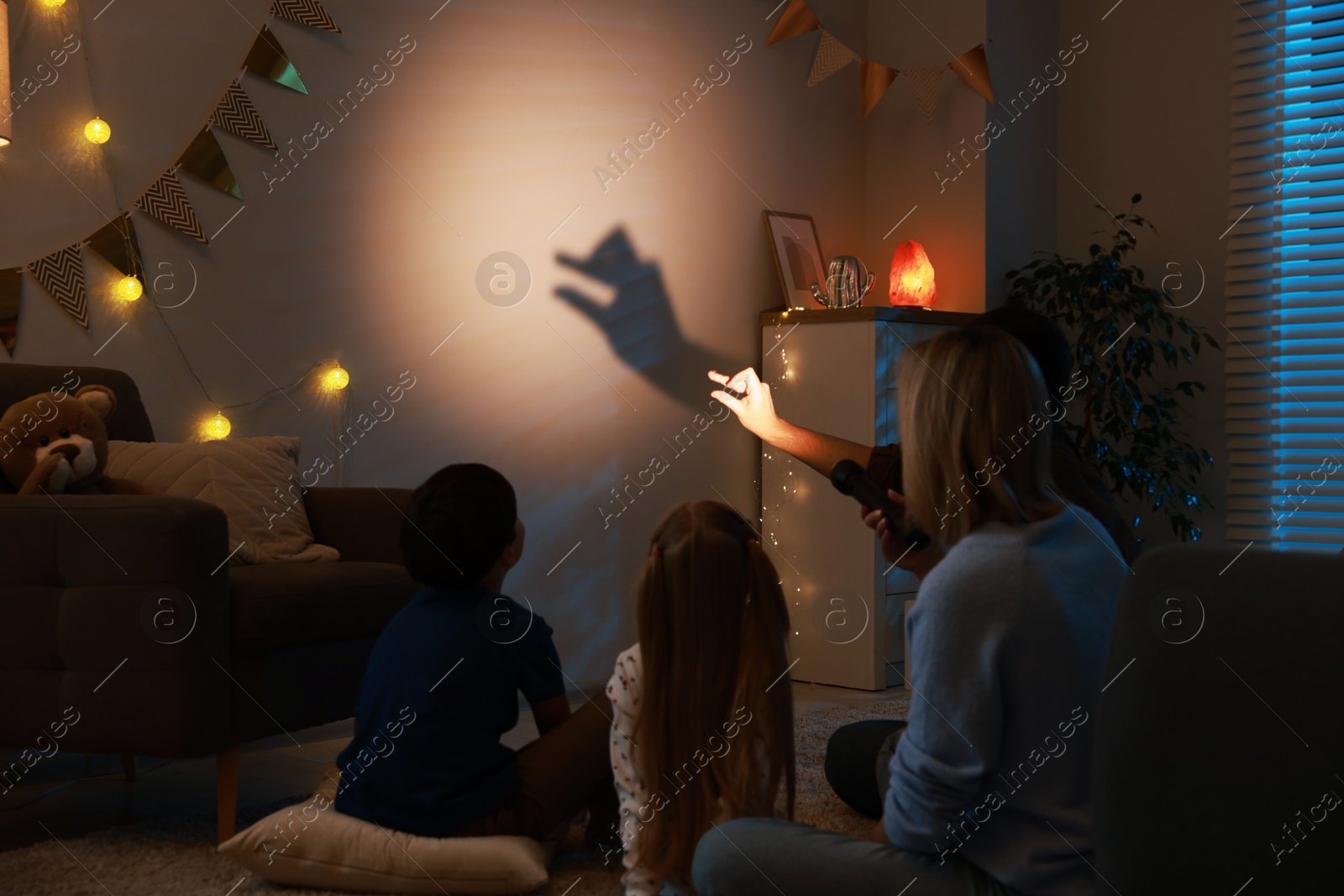 Photo of Man making hand gesture like goose while performing shadow play to his family at home, back view