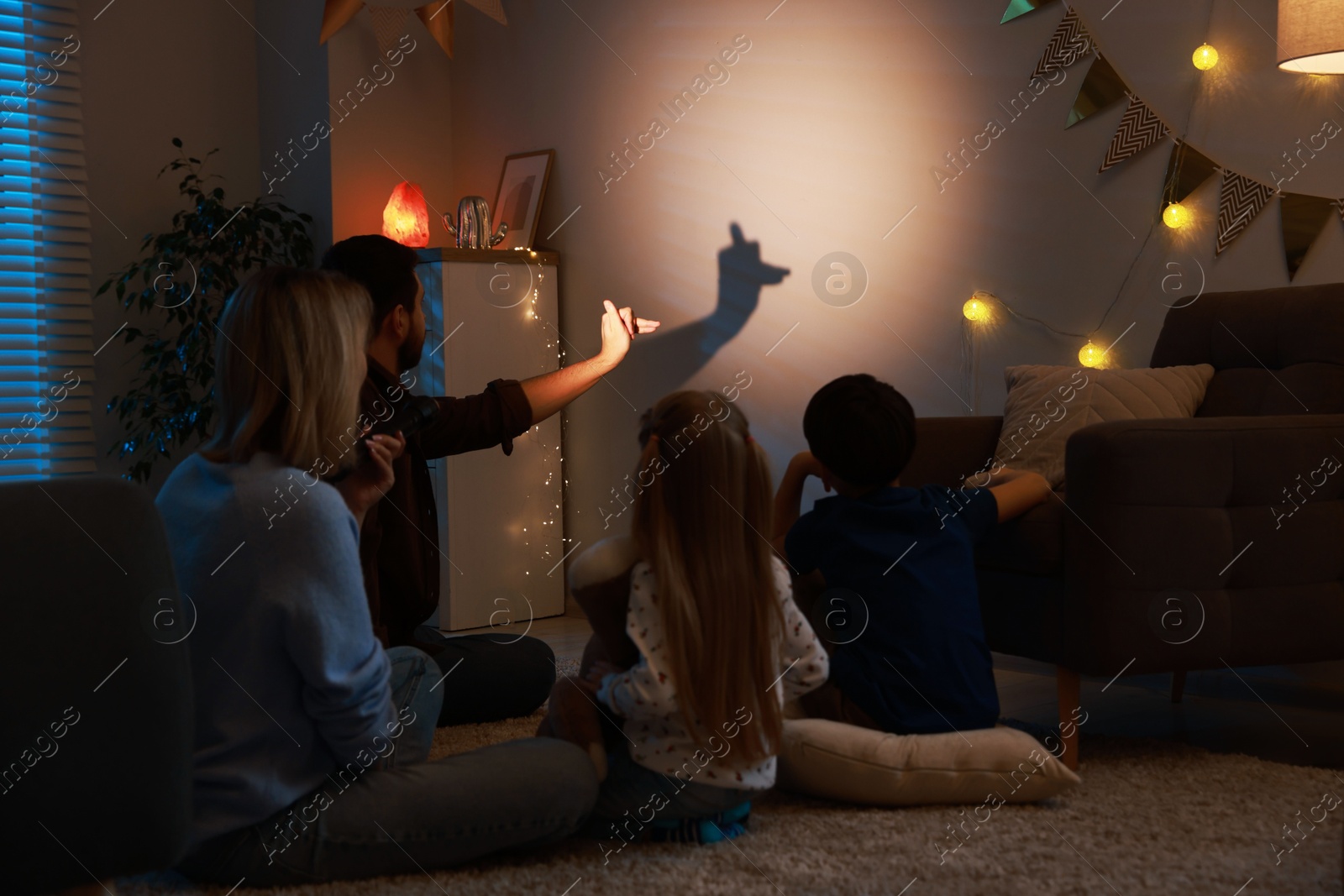 Photo of Man making hand gesture like llama while performing shadow play to his family at home