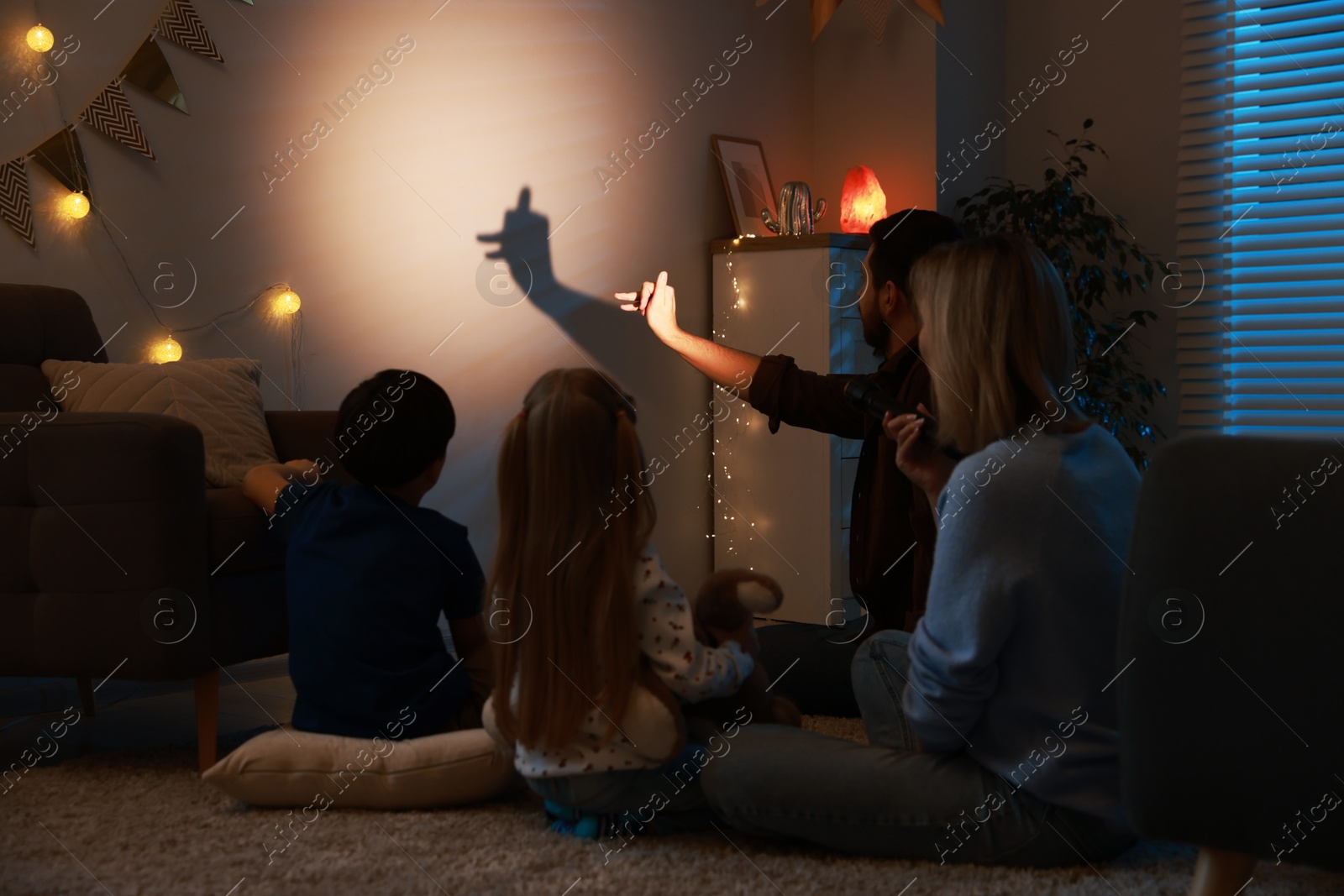 Photo of Man making hand gesture like llama while performing shadow play to his family at home