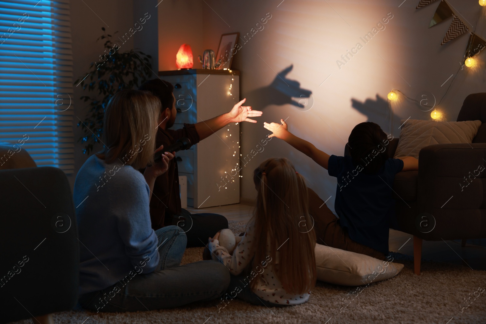 Photo of Shadow play. Father and his son making hand gestures like dogs on wall at home