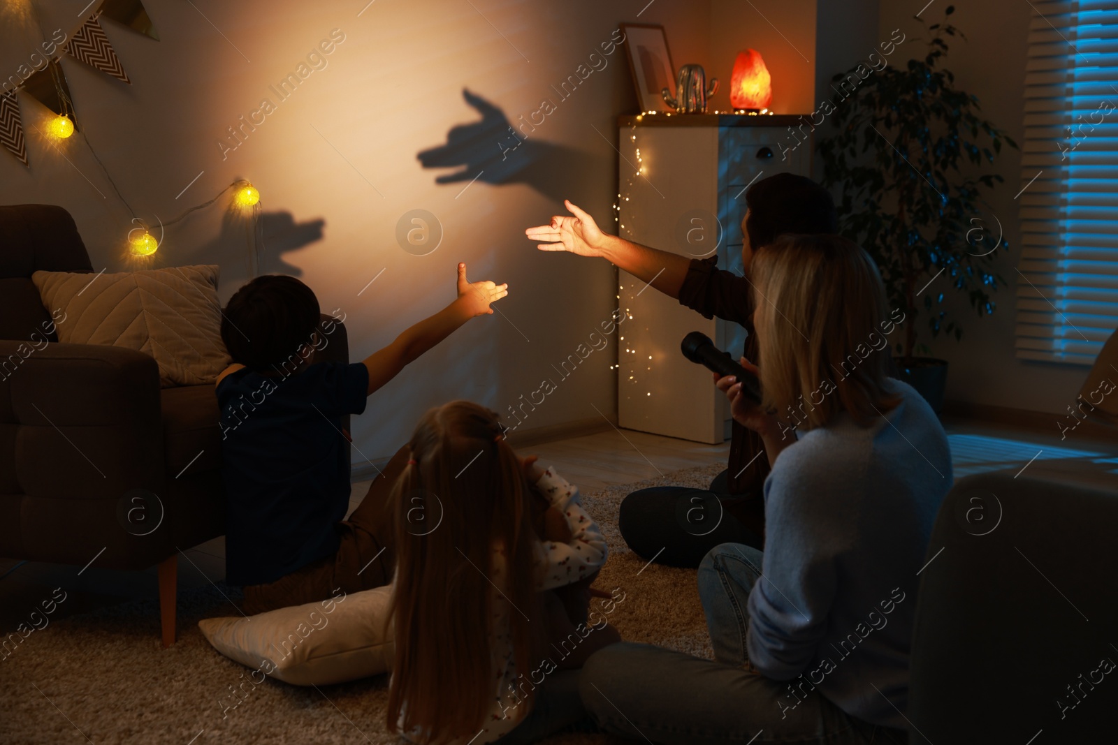 Photo of Shadow play. Father and his son making hand gestures like dogs on wall at home