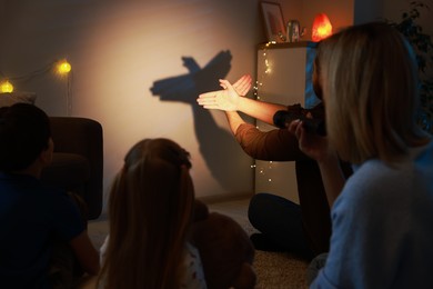 Photo of Man making hand gesture like bird while performing shadow play to his family at home