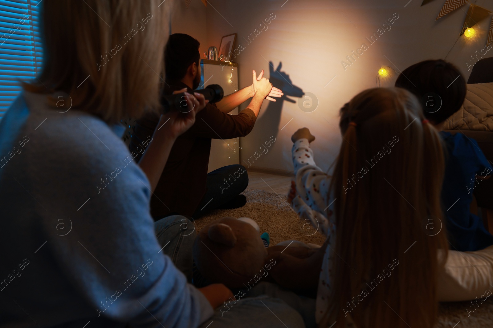 Photo of Man making hand gesture like donkey while performing shadow play to his family at home